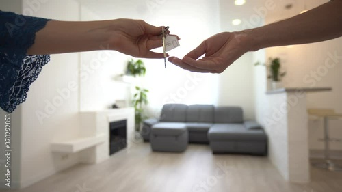 Close up of woman landlord giving keys of apartment to man tenant and shaking hands in agreement. Real estate agent giving house keys to buyer over interior photo