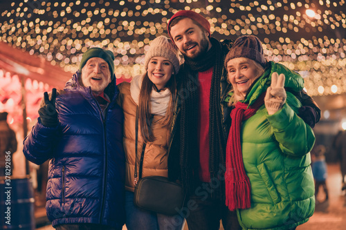 Portrait of nice attractive cheerful family embracing having fun spending time visiting street city urban market newyear tradition wintertime showing v-sign outside outdoor