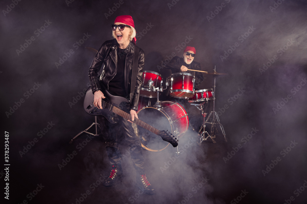 Full size photo of two cool aged lady man rock group performing concert drum instruments play solo guitar fog in air wear trendy rocker leather outfit bandana isolated black color background