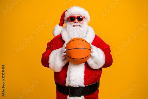 Portrait of his he nice attractive cheerful cheery sporty Santa holding in hands orange ball season team league isolated over bright vivid shine vibrant yellow color background