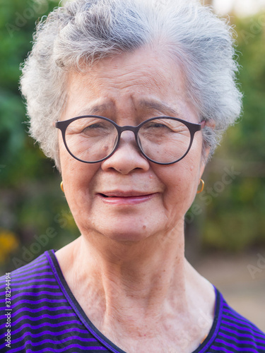 Portrait of an elderly Asian woman wearing eyeglasses looking at camera while standing in a garden