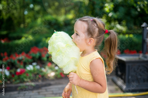 Cute toddler girl eating big yellow candyfloss or cotton candy  in the park on a summer sunny day.  photo