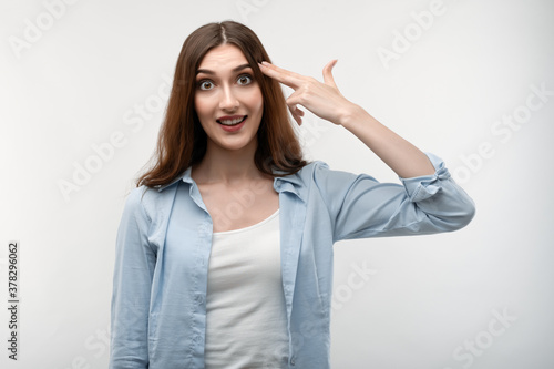 Fotografie Joyful Young woman foolishness imitates gun shoot keeps two fingers on temples