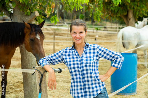 Photographie Happy confident young woman horses breeder standing near fencing of stable outdo