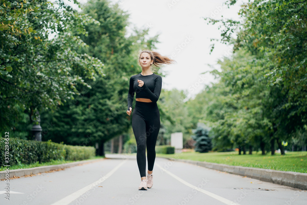 determined brunette woman of Caucasian appearance. running sports on a cross-country road. stylish tight comfortable clothing. nice weather summer day