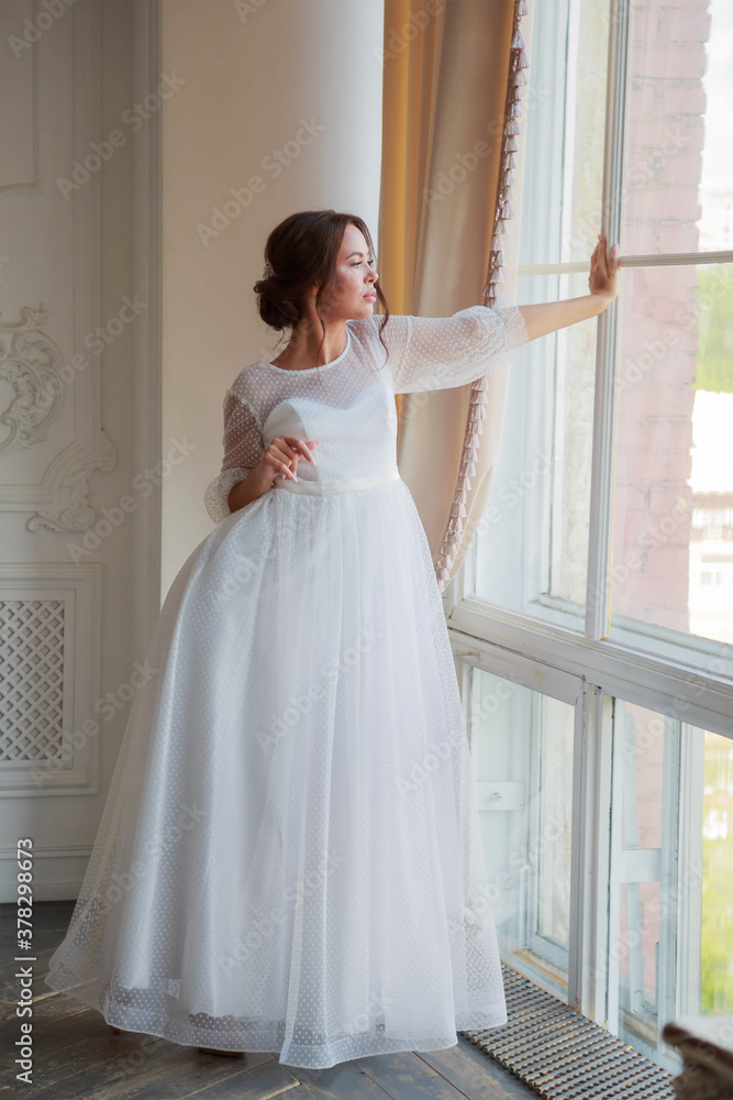 Full-length portrait of the bride in a white wedding dress by the window Full-length portrait of the bride in a white wedding dress by the window