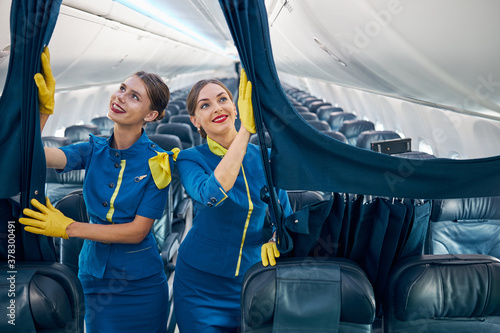 Beautiful females air hostesses in blue uniform with yellow scarf and gloves preparing plane to the passenger photo