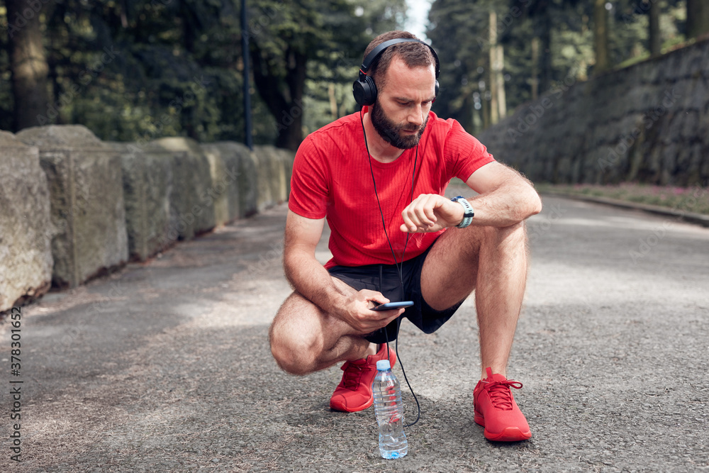 Tired sporty adult man kneeling after jogging and exercising in the park. Tired sporty adult man kneeling after jogging and exercising in the park.
