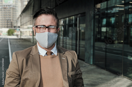 Portrait of businessman in eyeglasses and in protective mask looking at camera while standing in the city