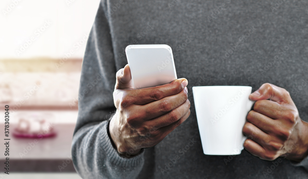 Man hands holding a coffee mug with phone inside of a house Man hands holding a coffee mug with phone inside of a house