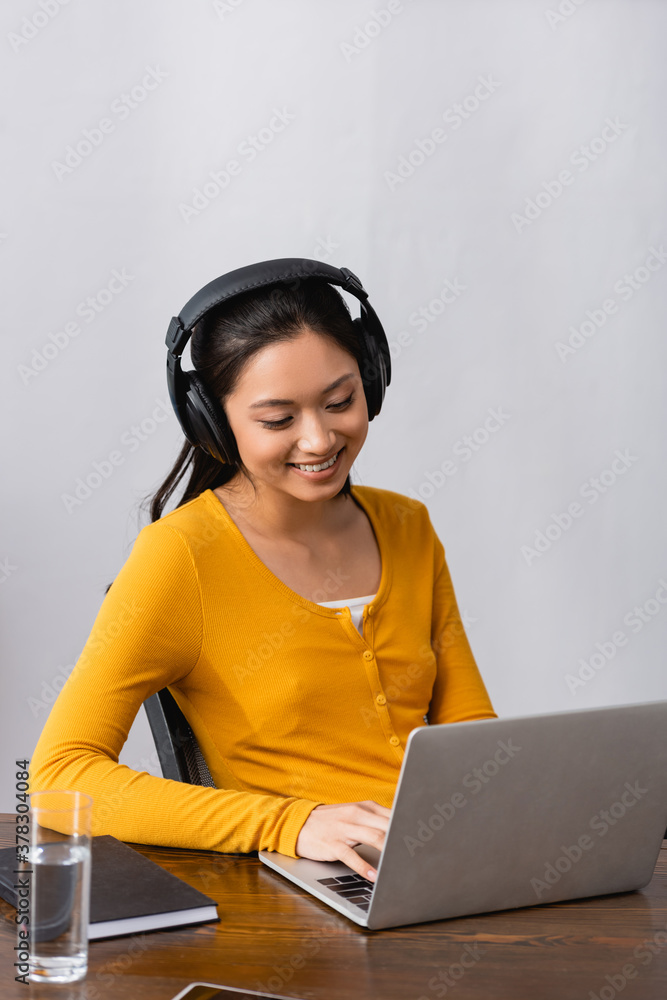 brunette asian freelancer in wireless headphones typing on laptop at home brunette asian freelancer in wireless headphones typing on laptop at home
