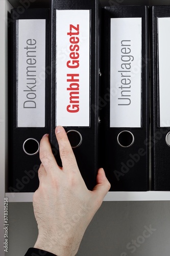 GmbH Gesetz. Ordner im Regal mit roter Beschriftung. Hand nimmt Dokumente aus Schrank im Büro