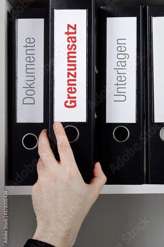 Grenzumsatz. Ordner im Regal mit roter Beschriftung. Hand nimmt Dokumente aus Schrank im Büro