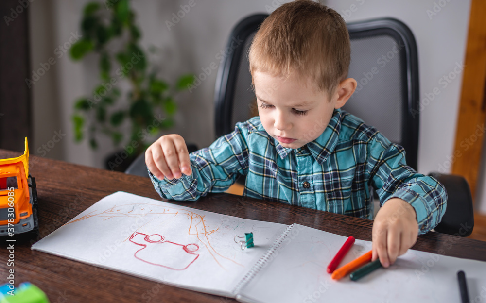 Cute child boy draws with chalk on paper in an album at the table. Preschool education and development of creativity Cute child boy draws with chalk on paper in an album at the table. Preschool education and development of creativity