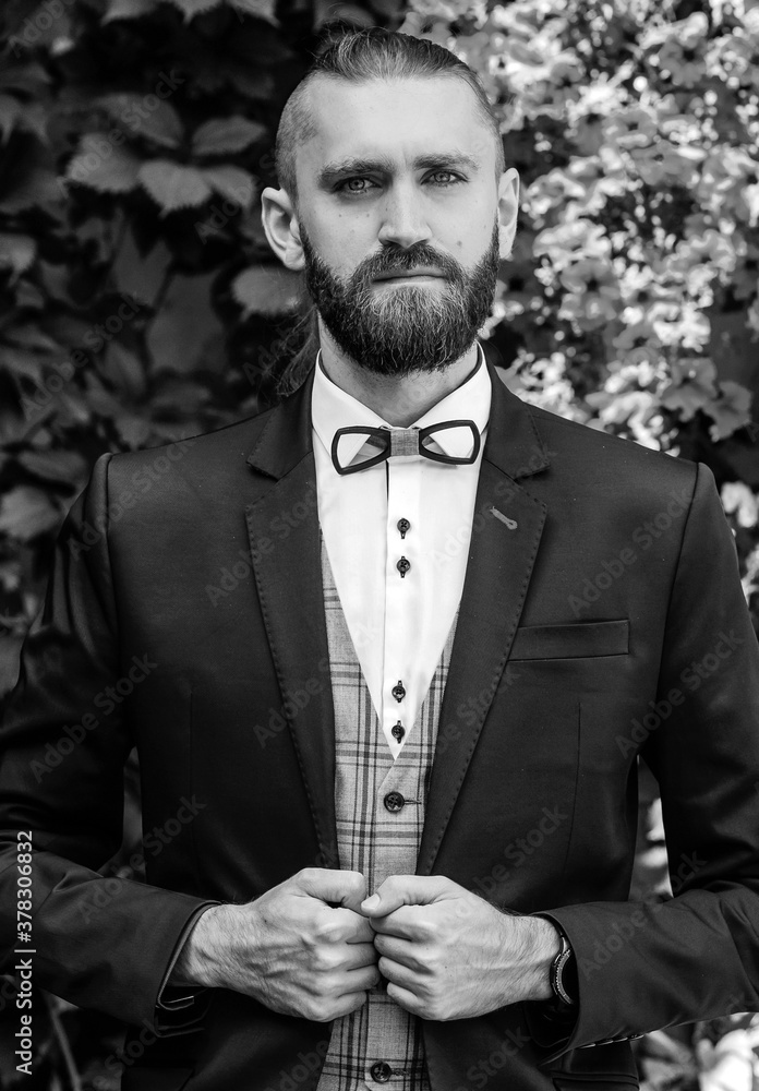 Fototapeta premium Black and white portrait bearded guy in a blue suit stands on the background of a flower wall
