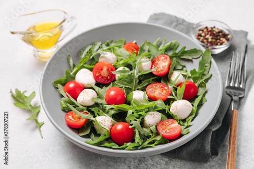 Diet and healthy salad with arugula, cherry tomatoes, mozzarella cheese and olive oil on white background