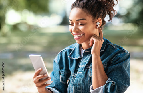 Black Millennial Girl Using Phone Making Video Call Siitting Outside photo
