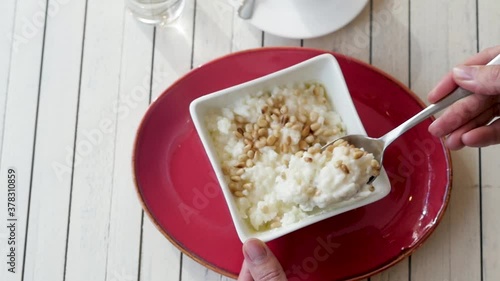 cup with rice on a white wooden background. breakfast of rice porridge. porridge in a red tarek on a white background. female hands take a spoonful of rice porridge with pine nuts. photo