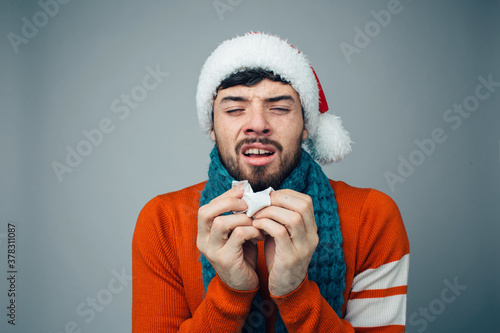 Young bearded man isolated over background. Guy in red festive clothes and hat suffer from running nose. Sneezing and caughing. Alone in studio. photo