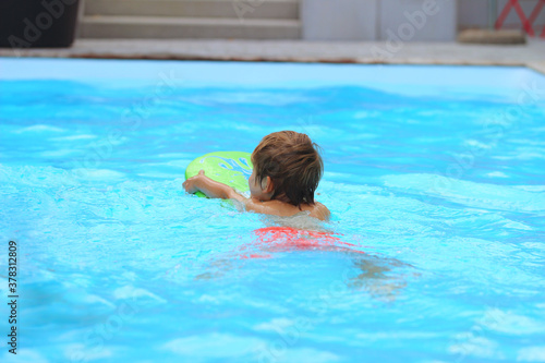 A boy swims with a swimming board in the pool. Relax, learn to swim and have fun. © Tsend-Ayush