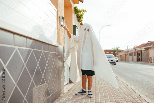 Child dressed as a ghost in halloween ringing the bell of his neighbors