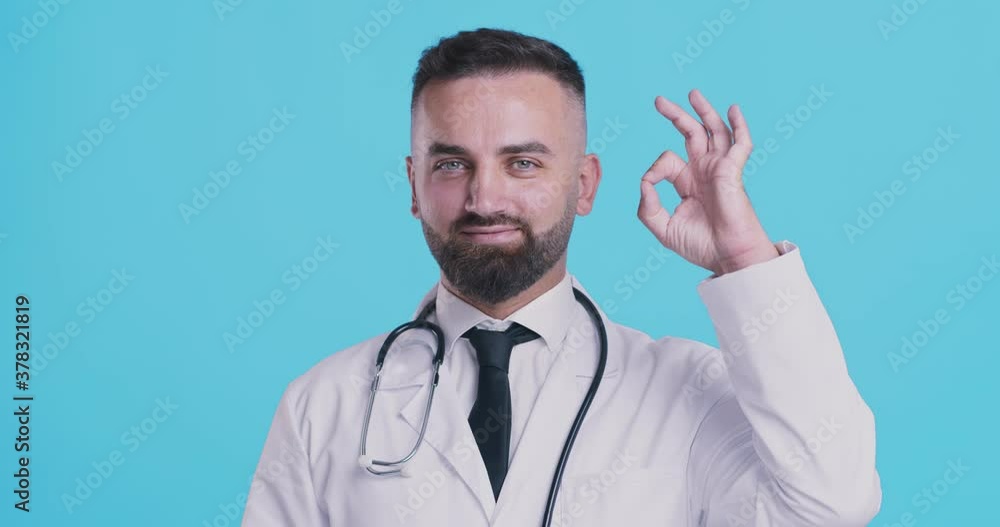 Positive medical doctor showing OK gesture, blue studio background Positive medical doctor showing OK gesture, blue studio background
