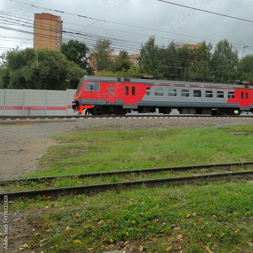 Moscow central diameter red gray electric train on railway near residential building on gray cloudy background at summer day
