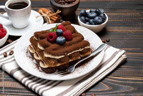 portion of Classic tiramisu dessert with raspberries. blueberries and cup of espresso coffee isolated on wooden background
