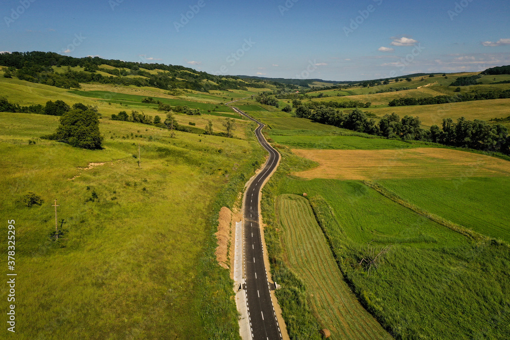 Naklejka premium Drone photograph with new asphalt road crossing a beautiful hilly landscape in summer season