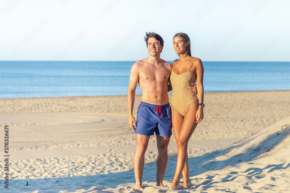 Young couple relaxing on the beach watching the sunset. Fit couple vacation.