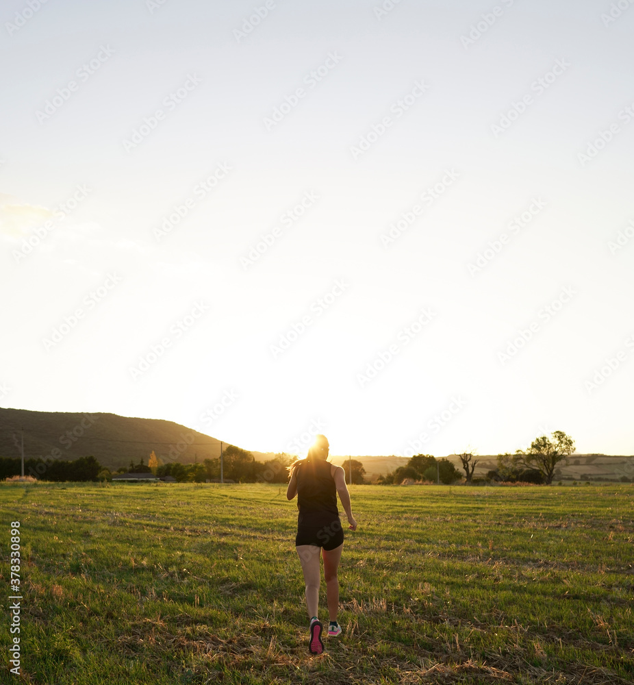 Young girl in black clothes and colorful sneakers running at sunset through a field