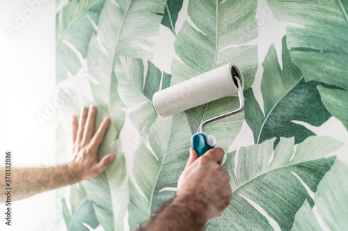 Tapezierer drückt die frisch verklebte Mustertapete mit der Rolle an die Wand 