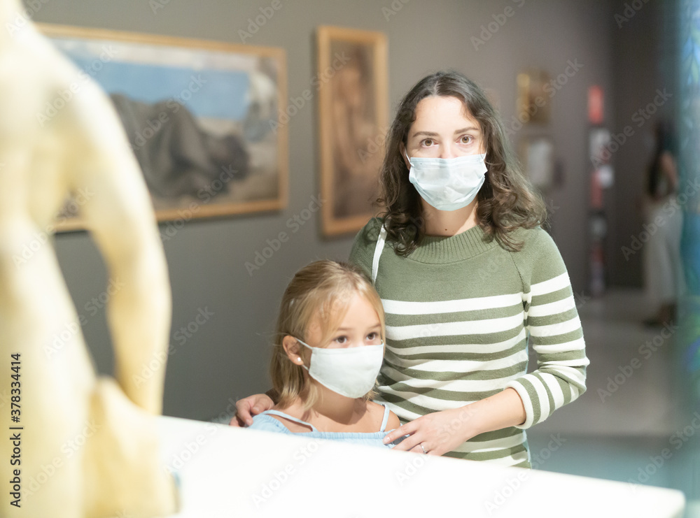 Girl with mother in masks looking with interest at art objects in museum