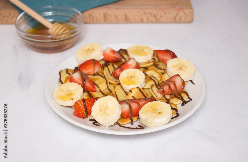 Trendy food - pancake cereal. Heap of mini cereal pancakes on a white plate, copy space. Strawberries, bananas, and honey. A beautiful and healthy Breakfast.
