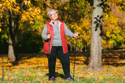 Obraz na płótnie Old woman resting in autumn park after nordic walking. Senior athlete outdoors w salonie