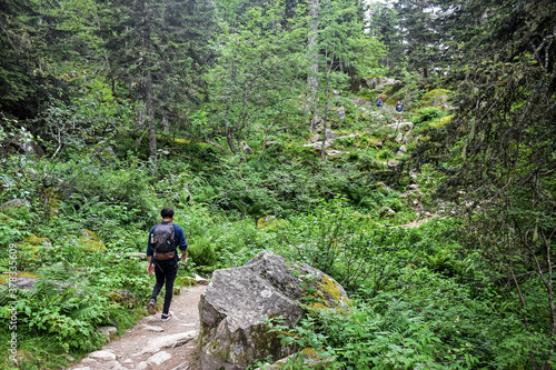 Young man with backpack walking on a hilly path surrounded by green nature 