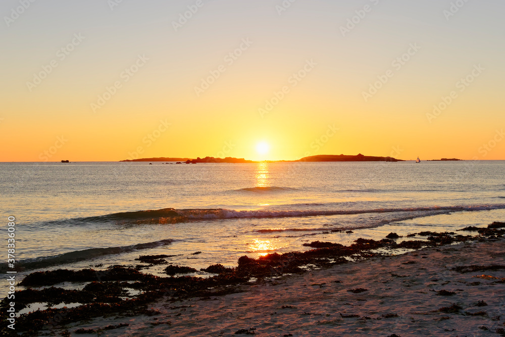 The summer sun sinks slowly between two small islands off the beach in Landeda, Brittany