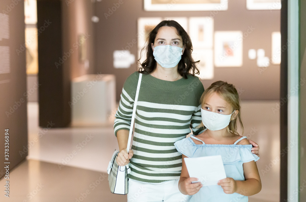 Mother and daughter in protective masks with guide enjoying expositions in museum