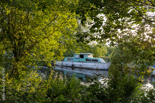 Boat moored on River lea towpath viewed through canalside sunlit trees at dusk photo