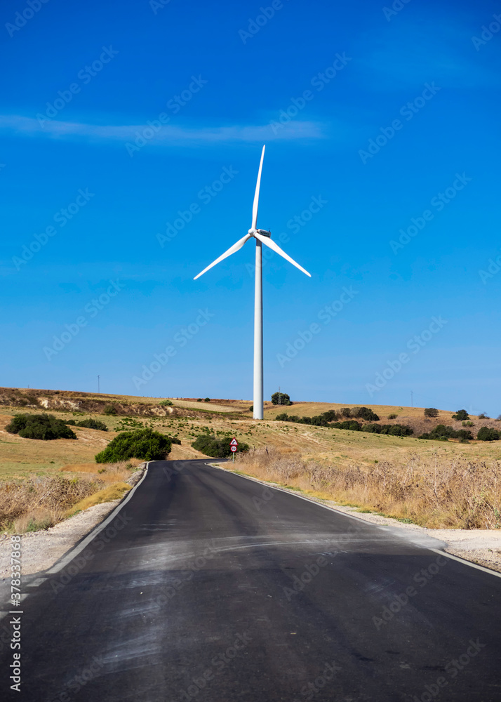 Una carretera solitaria pasa delante de un arogenerador de energia eólica.