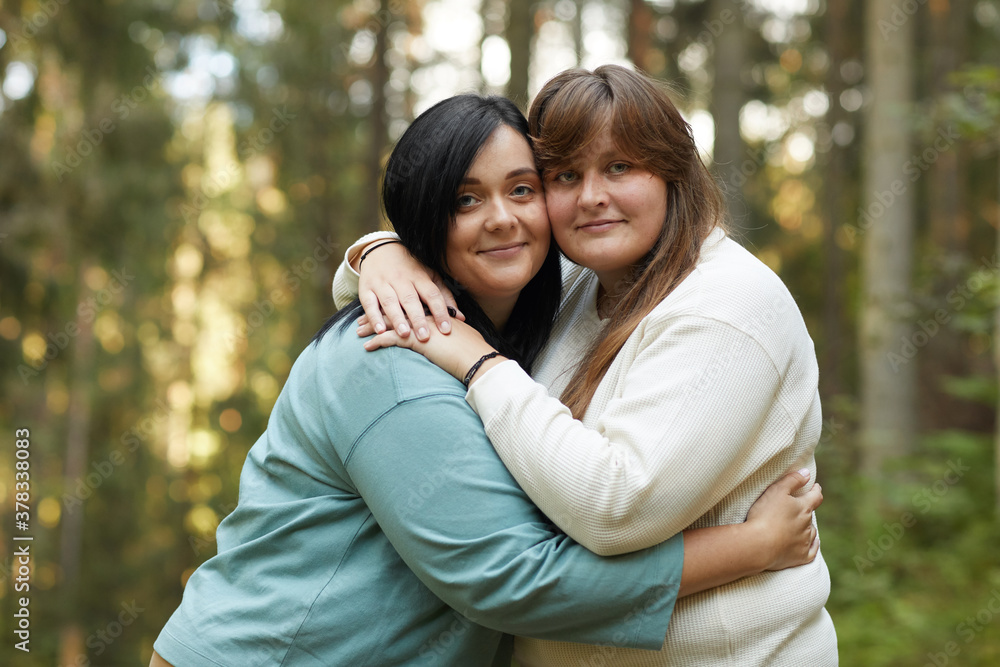 Portrait of two young lesbians embracing each other and smiling at camera while standing in the forest Portrait of two young lesbians embracing each other and smiling at camera while standing in the forest