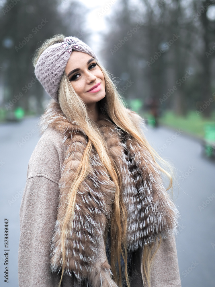 Blonde girl posing at the winter city in a fur coat and a hat