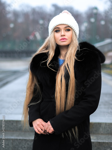 Blonde girl posing at the winter city in a black fur coat and a white hat © Sergii Mironenko