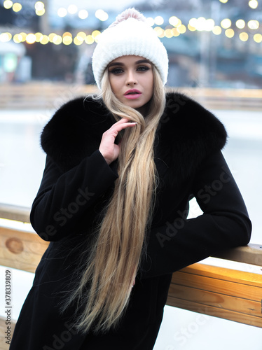Obraz na płótnie Blonde girl posing at the winter city in a black fur coat and a white hat w salonie