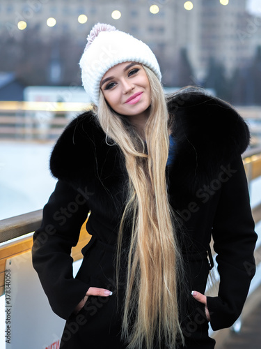 Obraz na płótnie Blonde girl posing at the winter city in a black fur coat and a white hat w salonie