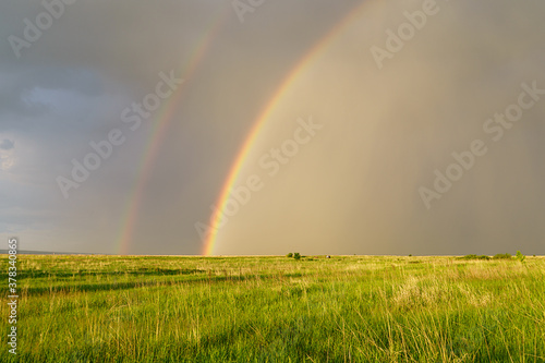 Summer landscape with a double rainbow over a field in a thunderstorm