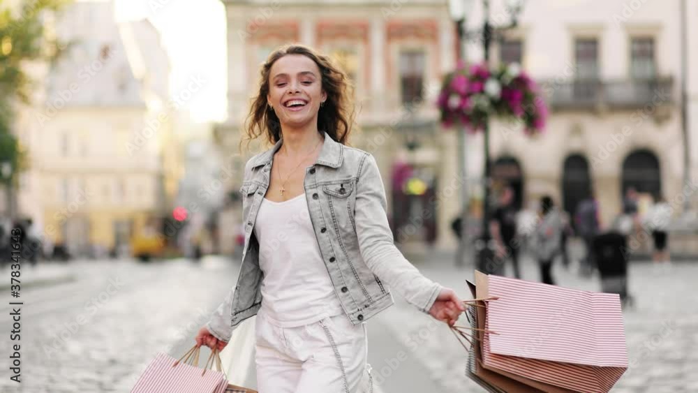 Charming blonde woman walking with shopping bags on city street in slow motion. Outdoor portrait happy female tourist having good time wandering around town in summer Charming blonde woman walking with shopping bags on city street in slow motion. Outdoor portrait happy female tourist having good time wandering around town in summer