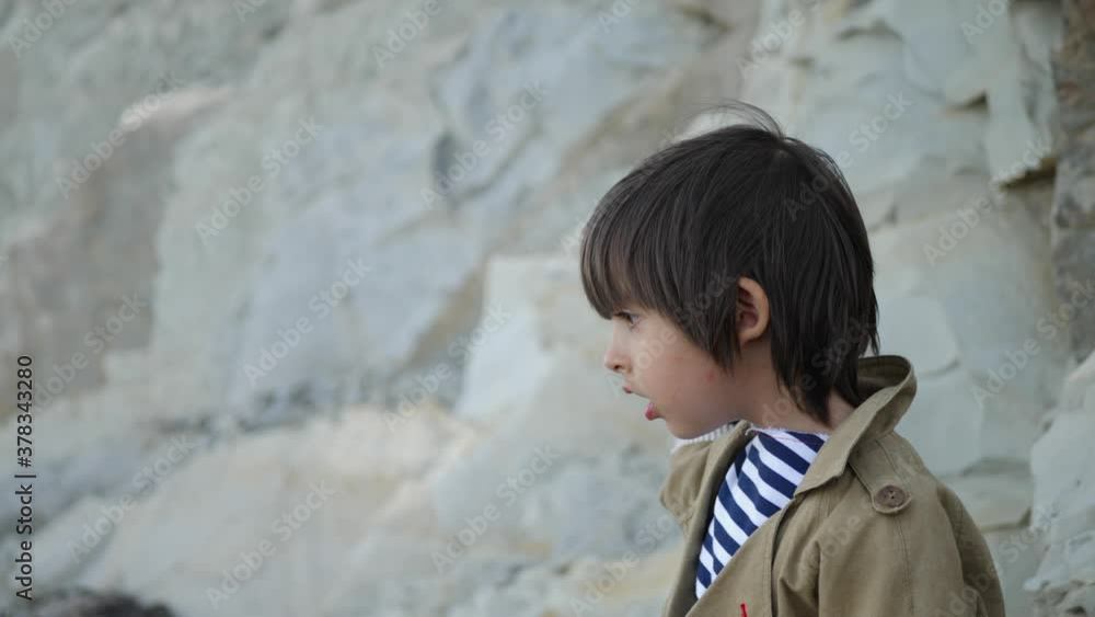 stylish boy child in red pants sit on a stone beach and looking for stylish boy child in red pants sit on a stone beach and looking for