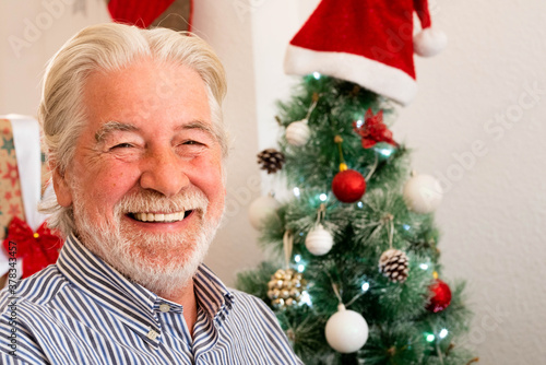 portrait and close up of old mature man smiling and laughing looking at the camera with a christmas tree at the background - old pensioner people at christmas day at home