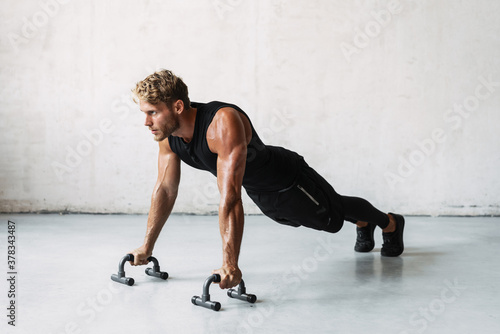 Obraz na płótnie Photo of athletic young sportsman working out with push-up stops